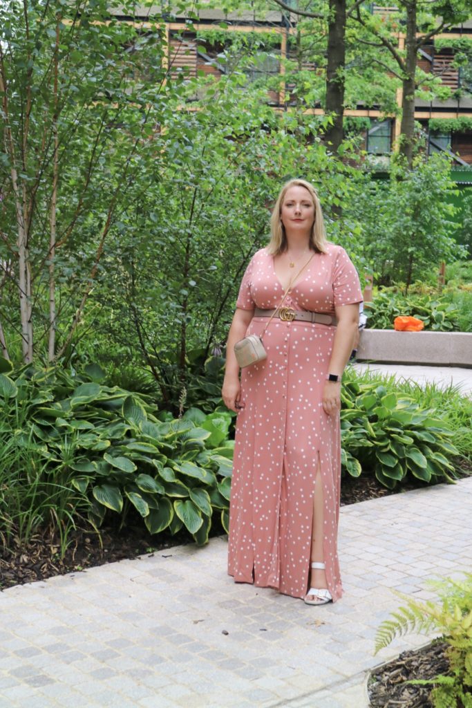 lucy stood in some gardens in mancheter in a pnk spotty maxi dress from ASOS