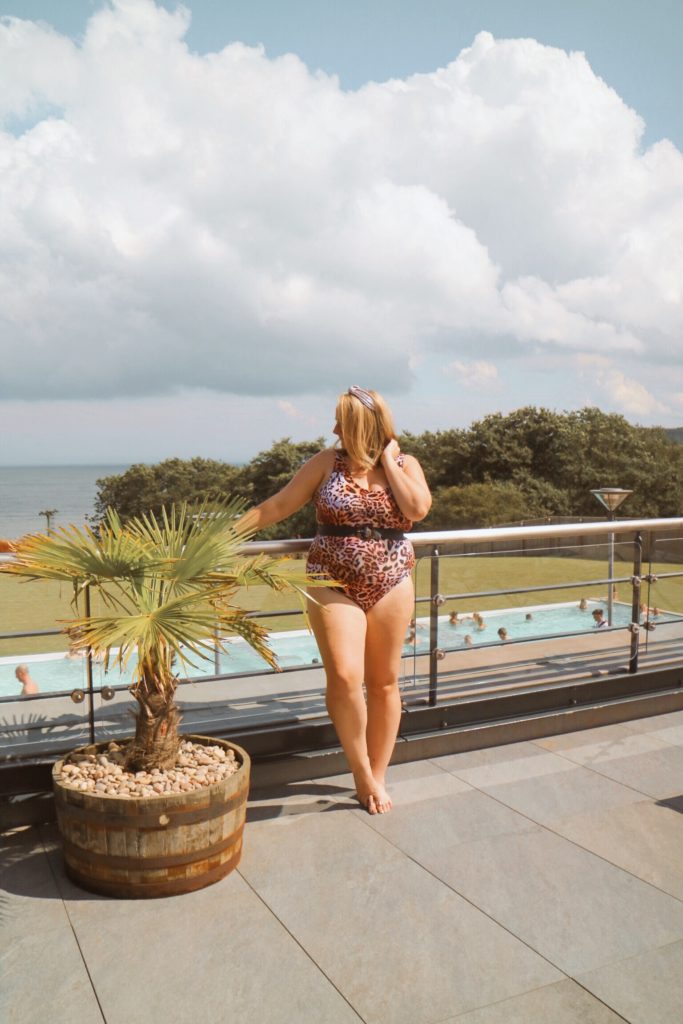 lucy in a leopard print swimming costume with the pool and sea below her