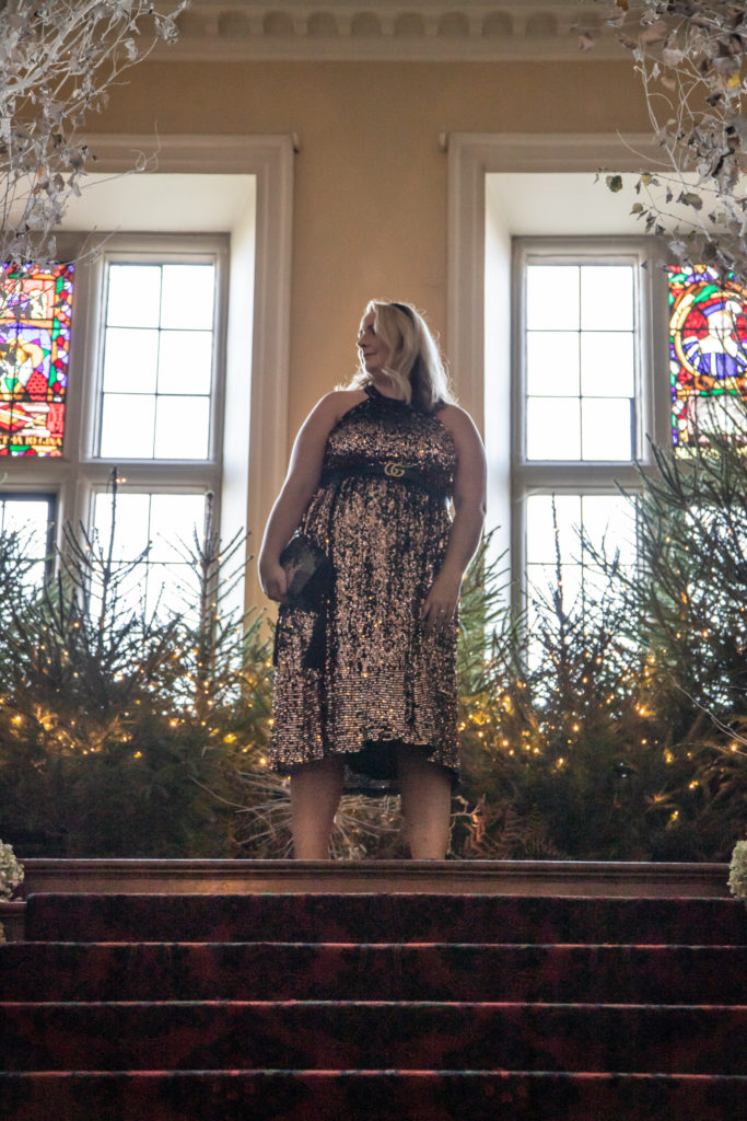 lucy in the sequin dress stood at the top os some stairs with stained glass behind
