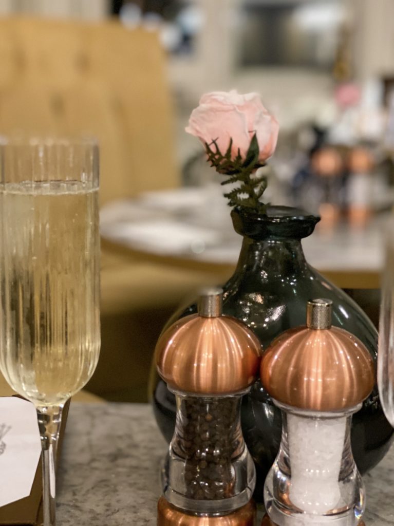 glass of champagne and rose in a vase with salt and pepper shakers in front