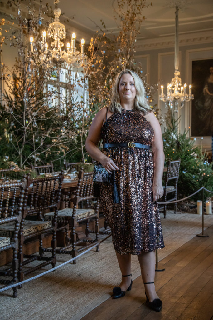 lucy in the sequin dress with a dining table behind and trees making a forest