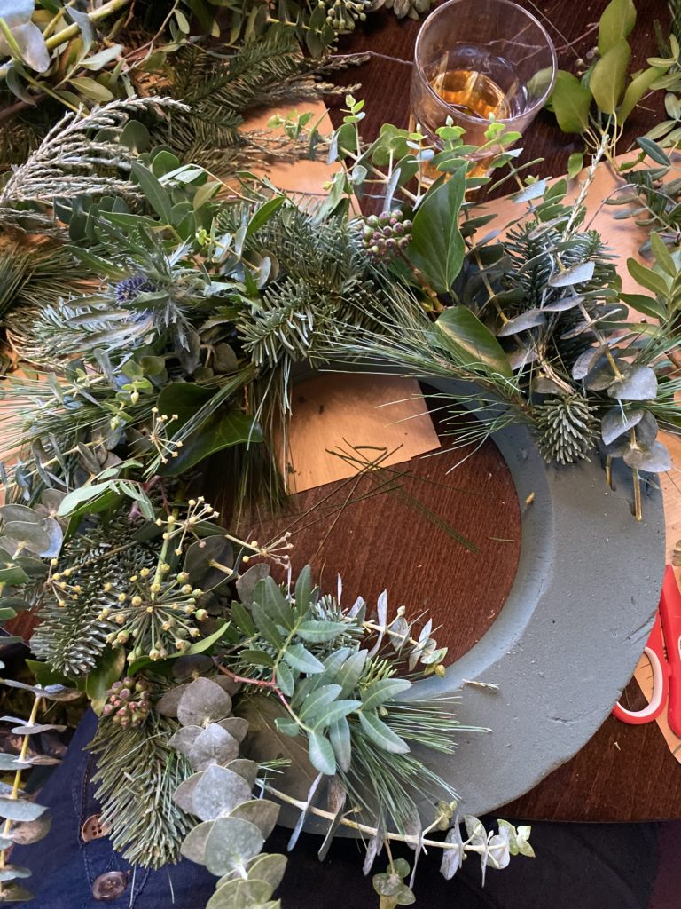 an oasis ring with foliage placed around some of it- a wreath in progress