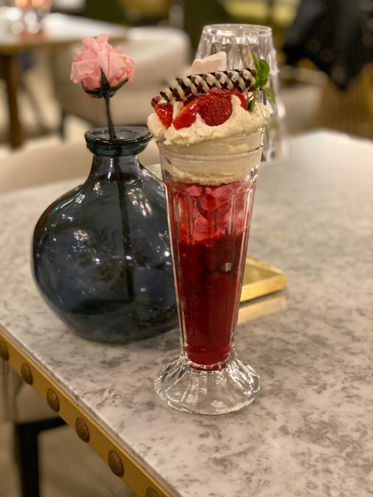a large sundae with a red sauce and cream on top with strawberries