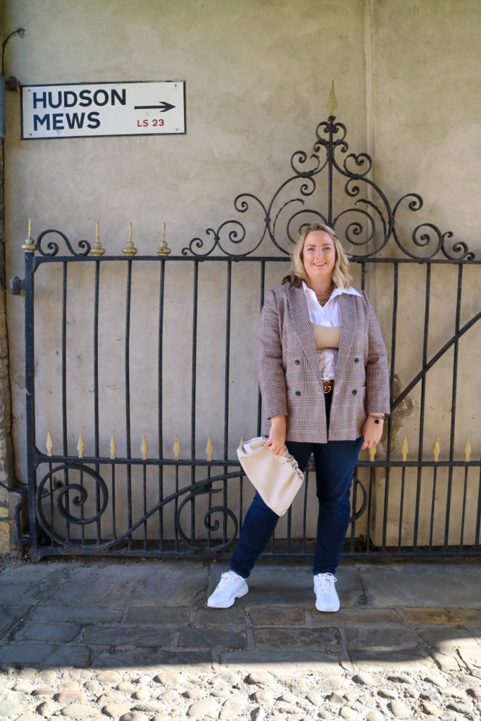 lucy stood in front of a scroll gate wearing a blazer, shirt, jeans and a knit bandau top